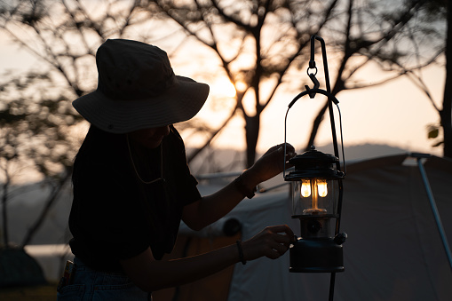 silhouette woman igniting lantern in camping tent on campsite. adjusting light up lamp in evening. lifestyle camper.