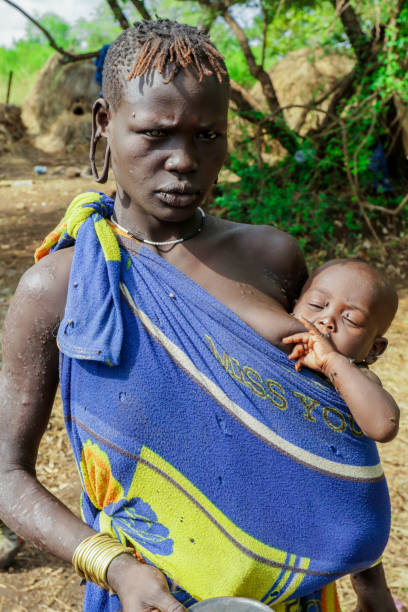 porträt einer afrikanischen frau mit einem säugling in blauer und gelber kleidung im lokalen mursi-stammesdorf - mursi tribe people ethiopia mother the human body stock-fotos und bilder