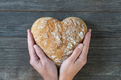 food, bread like a heart in woman hands on wooden table, essential for life