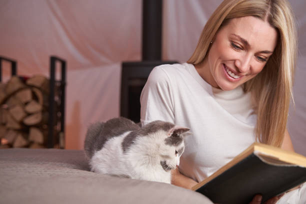 istock Pleased woman reading book with cat by her side 1361514096