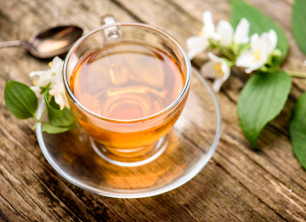 vaso de té de hierbas caliente en primer plano de fondo rústico. taza de té con té verde orgánico y flor de jazmín fresco sobre mesa de madera. medicina alternativa saludable y bebida natural de desintoxicación. - tea tea leaves jasmine tea leaf fotografías e imágenes de stock