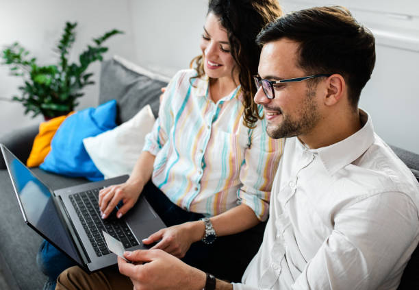istock Smiling couple sitting on sofa using laptop in hotel room. 1361515946