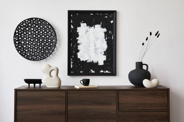 istock Creative composition of modern living room interior design with mock up poster frame, brown commode, vases, sculpture and personal accessories. White wall. Copy space. Template.