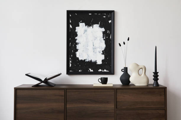 istock Creative composition of modern living room interior design with mock up poster frame, brown commode, vases, candlestick and personal accessories. White wall. Copy space. Template. 1361516030