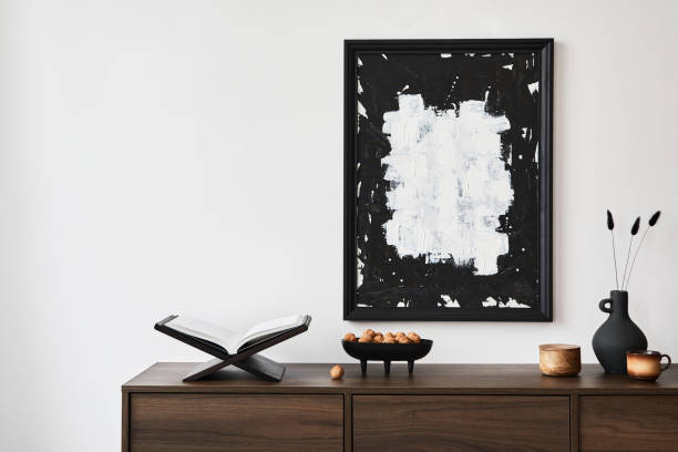 istock Creative composition of modern living room interior design with mock up poster frame, brown commode and personal accessories. White wall. Copy space. Template.