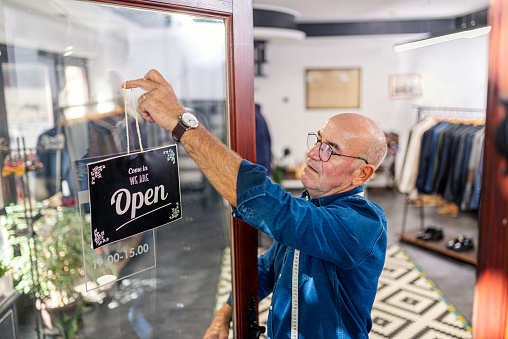 Close up photo of a professional tailor putting an open sign on tailoring store door