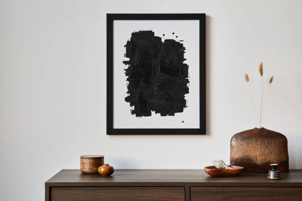 istock Creative composition of modern living room interior design with mock up poster frame, brown commode, vases and personal accessories. White wall. Copy space. Template.