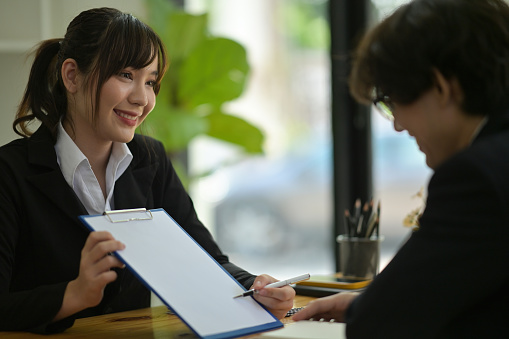 Photo of a young businesswoman offers a business plan to her colleague at the wooden working desk.