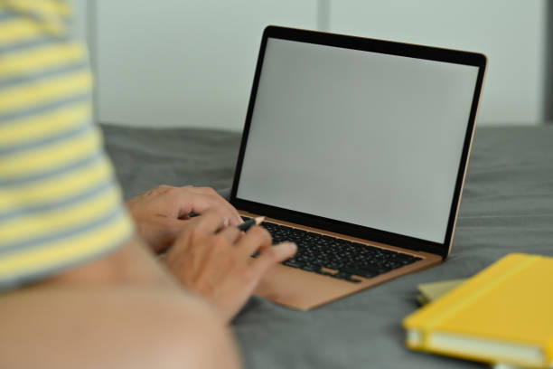 istock Cropped image of a young man typing on a white blank screen computer laptop on his bed. 1361531284