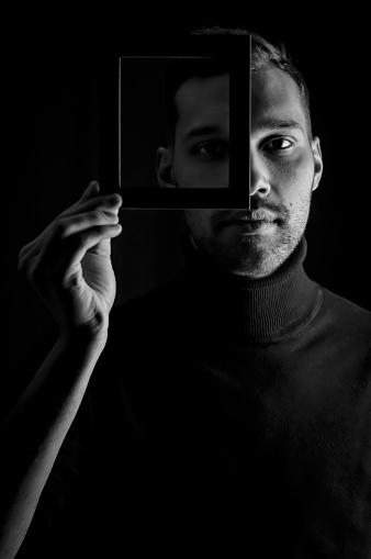 portrait of a young man holding a frame in front of his face, concept for the uniqueness of individuals