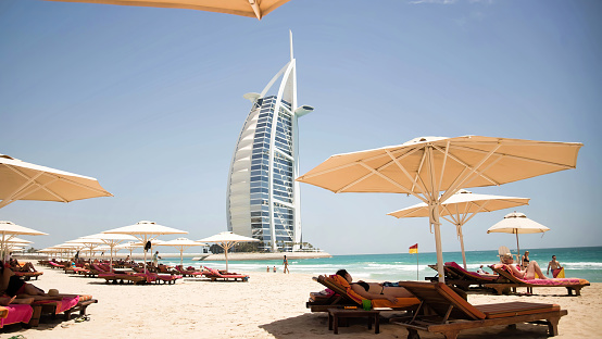 Dubai, UAE - May 2013: People enjoying a sunny day at Jumeirah beach in front of the Burj al Arab hotel. Jumeirah Beach is a white sand beach that is located and named after the Jumeirah district