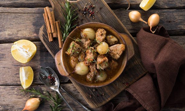 stifado - delicious mediterranean beef stew with onion bulbs, cinnamon and spices in a casserole, on a black wooden table, view from above, close-up stock photo