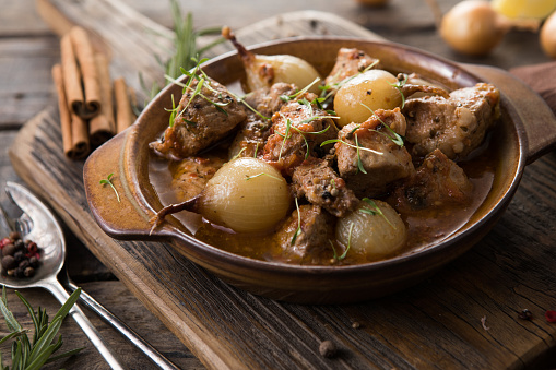 stifado - delicious mediterranean beef stew with onion bulbs, cinnamon and spices in a casserole, on a black wooden table, view from above, close-up