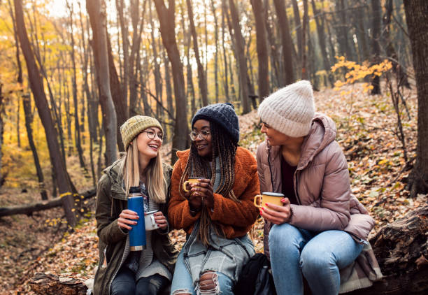 istock Three female friends resting after hiking in forest sitting on collapsed trunk and drinking tea. 1361550066