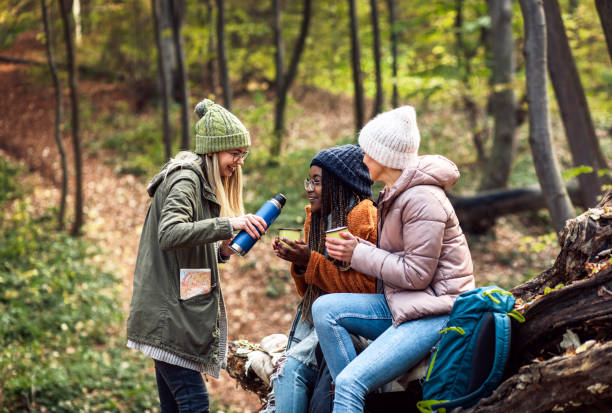 istock Three female friends resting after hiking in forest sitting on collapsed trunk and drinking tea. 1361553864