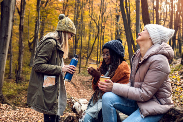 istock Three female friends resting after hiking in forest sitting on collapsed trunk and drinking tea. 1361553928