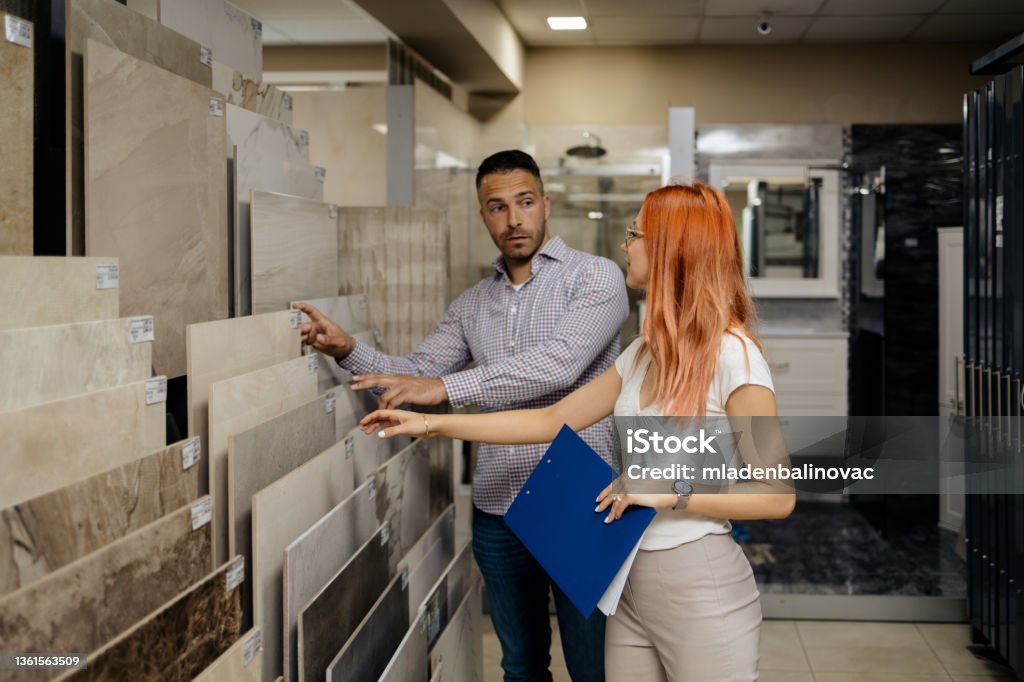 Bathroom tiles and utensils shopping Elegant middle age businessman choosing ceramic tiles and utensils for his home bathroom and female seller helps him to make right decision Tiled Floor Stock Photo