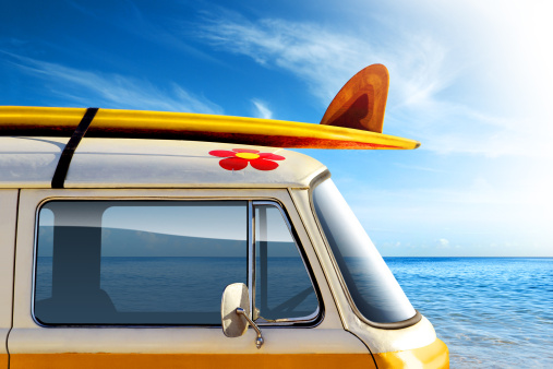 Detail of a vintage van in the beach, with a surfboard on the roof.