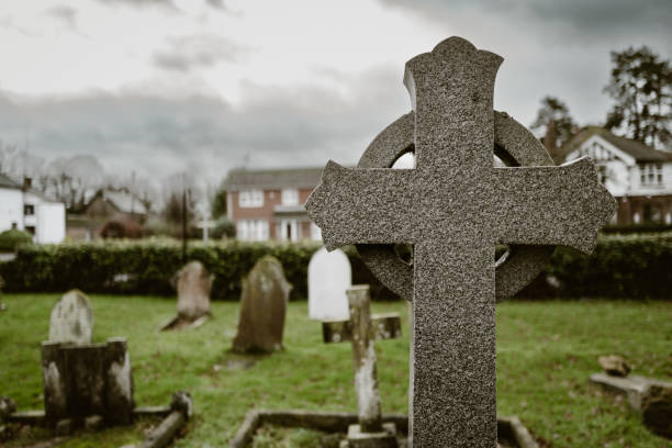 Shallow focus of a granite constructed religious cross marking an ancient grave in a typical English cemetery. Shallow focus of a granite constructed religious cross marking an ancient grave in a typical English cemetery. Distant large houses can be seen in the centre of the village. funeral planning stock pictures, royalty-free photos & images