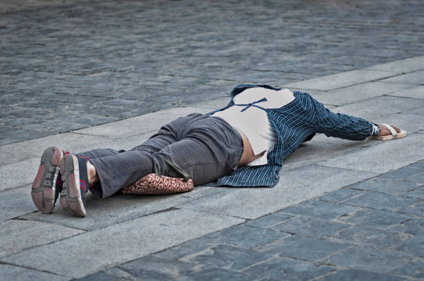 Addis Abeba, Ethiopia, 07/10/2007.A semi-naked beggar sleeps on the ground in the middle of a pedestrian zone on a street. The shirt is spread out on the ground, held by a stone and has coins thrown by passers-by, one of them is stuck to the skin after changing position. Well-dressed people passing by and observing the scene. Two children who look at him openly with an expression of fright and concern. In the background, street vendors of cotton packages with cardboard boxes as a stall. Red painted fences that surround the urban area and residential buildings.