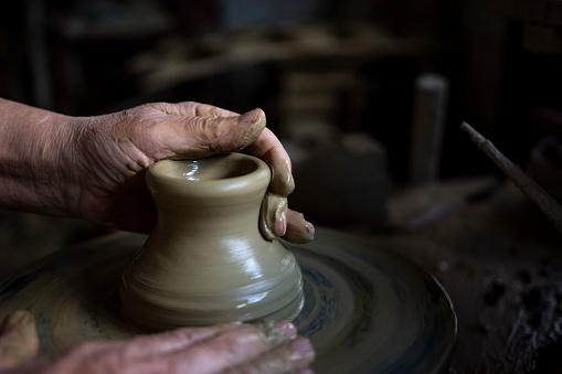Potter's hands work a small earthenware jug on a potter's wheel
