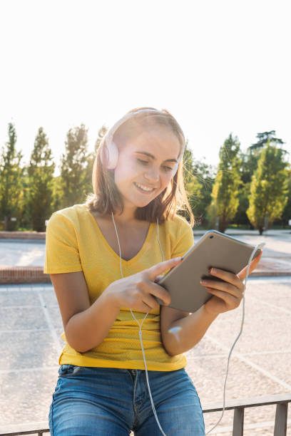 Young blond hair girl wearing yellow t-shirt, smiling and looking at her tablet, with the sun behind. Technology, lifestyle and relaxation concept stock photo