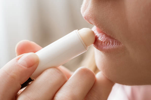 young woman applies moisturizing balm to her lips - cheek color imagens e fotografias de stock