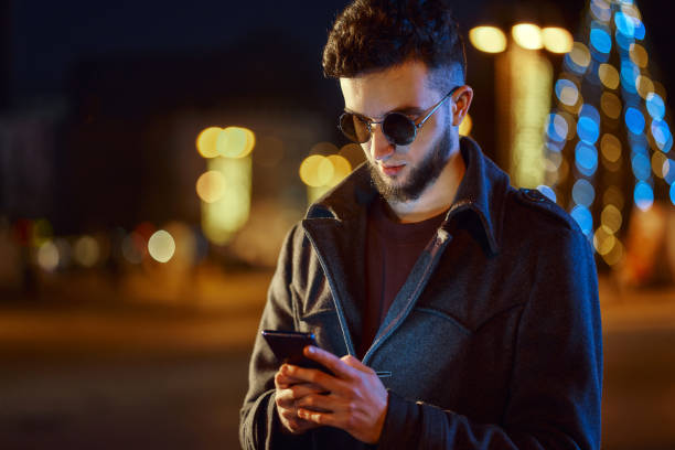 istock Handsome man with glasses using smartphone in night city street 1361583833