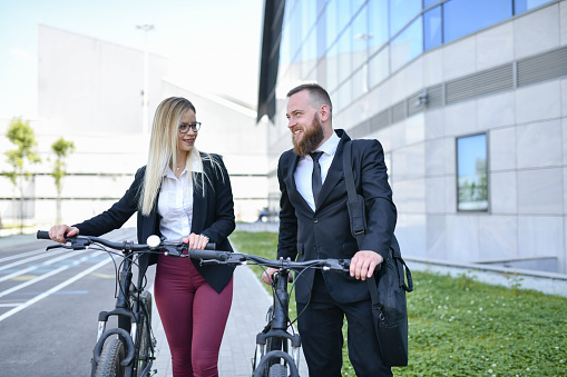 Bearded Businessman Flirting With Elegant Female While Pushing Bicycles Outside