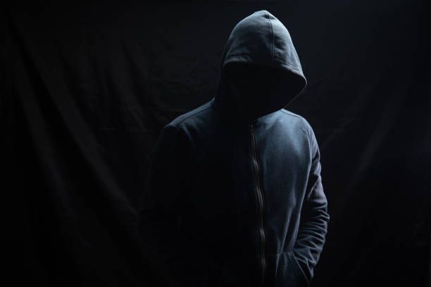 istock a man in a hood stands on a black background 1361592105