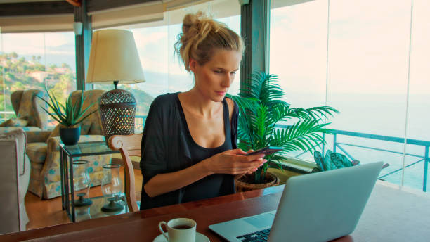 istock Woman working by panoramic windows. Using laptop and having coffee with epic sea view 1361593397