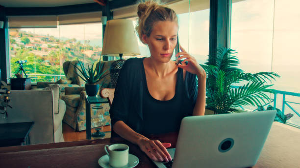 istock Woman working by panoramic windows. Using laptop and having coffee with epic sea view 1361593422