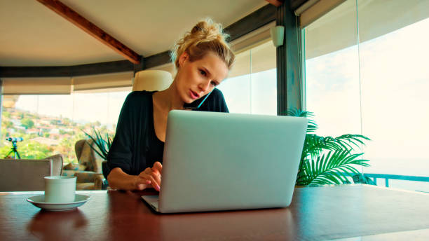 istock Woman working by panoramic windows. Using laptop and having coffee with epic sea view 1361593553