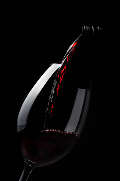 Red wine pouring into wine glass on dark background stock photo