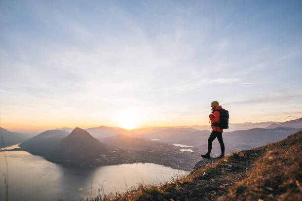 Female hiker relaxes on grassy mountain ridge at sunrise She looks out over Lake Lugano and the Swiss Alps in the distance lugano stock pictures, royalty-free photos & images