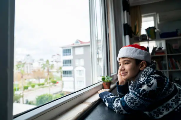Photo of Photo Of Boy Wearing Santa Hat And Christmas Themed Sweater Looking Through Window