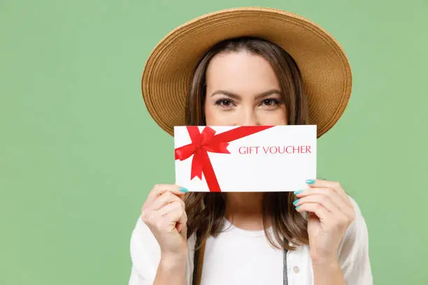 Traveler tourist woman in casual clothes hat camera cover mouth with gift voucher flyer mock up isolated on green background Passenger travel abroad on weekends getaway. Air flight journey concept.