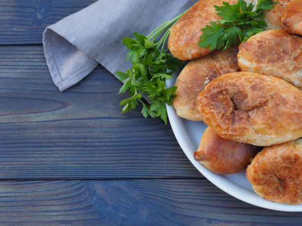 Fried pies with cabbage in a plate with a napkin, herb parsley on a dark wooden table, closeup, top view, flat layout, copy space. Traditional delicious hot snack pirozhki. Russian, Ukrainian cuisine pasteles fritos con repollo en un plato con una servilleta, perejil de hierbas en una mesa de madera oscura, primer plano, vista superior, diseño plano, espacio de copia. delicioso bocadillo caliente tradicional pirozhki. cocina rusa, ucraniana