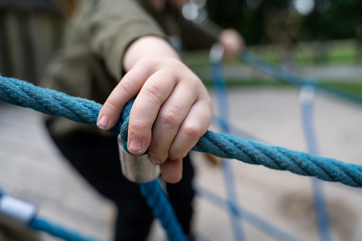 Boy is holding a blue rope while walking on a bridge in the playground. Taken in daytime.
