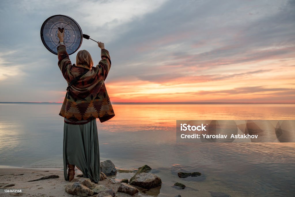 Young ethnic mature shaman female is walking and playing drums meditative music Shaman Stock Photo