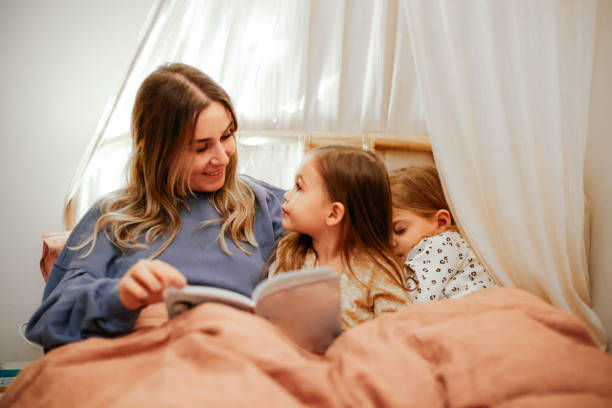 istock Mother and daughters reading book in bed before going to sleep 1361612239