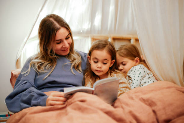 istock Mother and daughters reading book in bed before going to sleep 1361612321