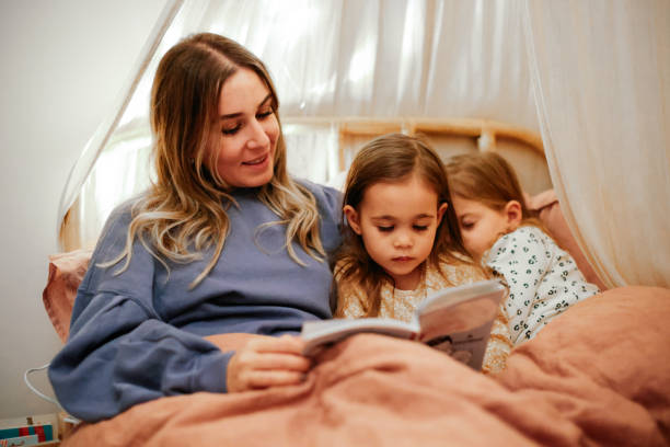 istock Mother and daughters reading book in bed before going to sleep 1361612387