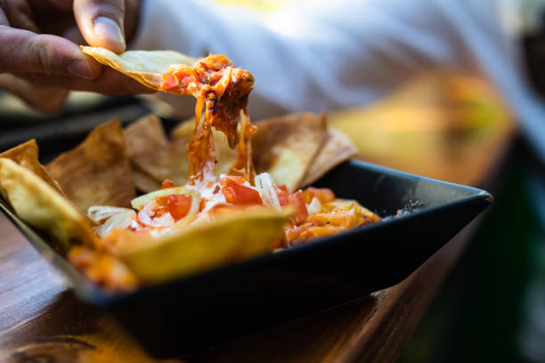 A cropped shot of a man's hand scooping nacho sauce with a nacho