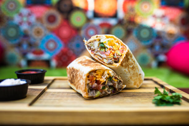 a burrito with dips cut in half on a wooden board - mexican dish imagens e fotografias de stock