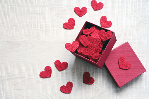 Open gift box and knitted hearts on light background, top view. Valentines day greeting card. Flat lay style.