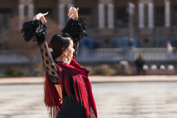 Woman in flamenco outfit raising arms while dancing outdoors stock photo