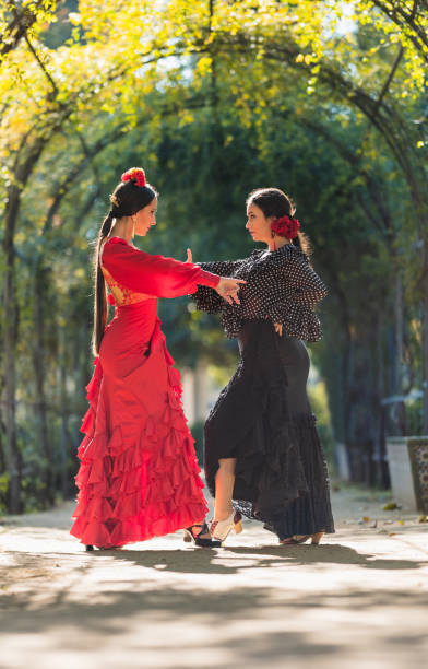 две женщины в платьях фламенко танцуют в окружении арки растений - танец фламенко стоковые фото и изображения