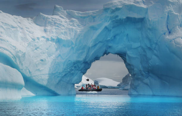 Antarctic tourists A small Zodiac inflatable boat carries tourists beneath a huge blue iceberg in the lagoons and bays surrounding the Antarctic peninsular antartica stock pictures, royalty-free photos & images