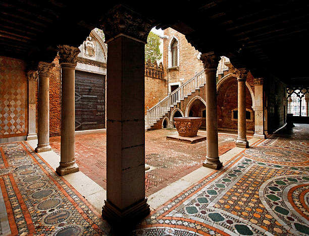 Venice, Italy - May 16, 2015: A quiet piazza with a lone female pedestrian and an old water well surrounded by yellow buildings in the Jewish Ghetto in Venice, Italy. The Venetian Ghetto is the oldest remaining ghetto in Europe, but fewer than 50 Jews still live there.